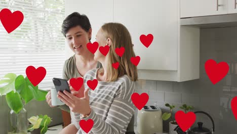 Animation-of-hearts-over-caucasian-female-couple-using-smartphone