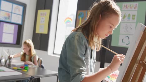 Video-of-concentrating-caucasian-schoolgirl-standing-at-easel-painting-in-art-class,-copy-space