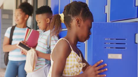 Video-portrait-of-happy-african-american-schoolgirl-using-locker-at-school