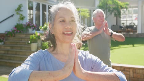 Happy-diverse-senior-couple-practicing-yoga-on-sunny-day-in-garden