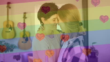 Animation-of-heart-emojis-and-rainbow-flag-over-caucasian-female-couple-embracing