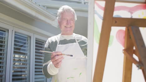 Happy-caucasian-senior-man-painting-in-garden-on-sunny-day