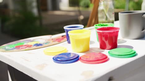Close-up-of-colourful-paints-and-painting-equipment-lying-on-table-in-garden