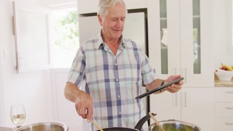 Glücklicher-Kaukasischer-älterer-Mann,-Der-Ein-Tablet-Benutzt-Und-In-Der-Küche-Kocht