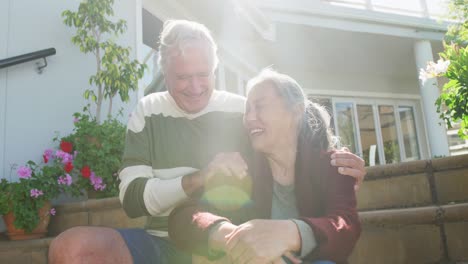 Happy-diverse-senior-couple-sitting-on-stairs-on-sunny-day-in-garden