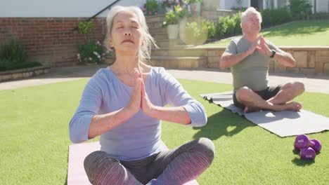 Glückliches,-Vielfältiges-älteres-Paar,-Das-Yoga-Praktiziert-Und-Auf-Matten-Im-Garten-Meditiert