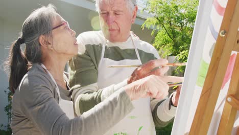 Happy-diverse-senior-couple-painting-in-garden-on-sunny-day