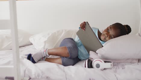 Smiling-african-american-girl-using-tablet-lying-on-bunk-bed-at-home,-copy-space