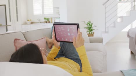 Asiatische-Frau-Benutzt-Tablet-Und-Liegt-Auf-Der-Couch-Im-Wohnzimmer