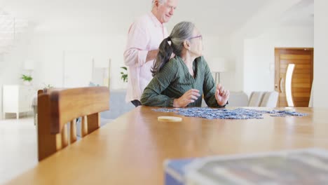 Happy-diverse-senior-couple-sitting-at-table-and-doing-puzzle