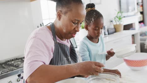 Happy-african-american-grandmother-and-granddaughter-baking-together-in-kitchen,-copy-space