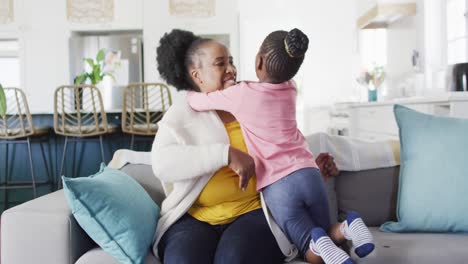 Happy-african-american-granddaughter-and-grandmother-hugging-on-couch-at-home,-copy-space