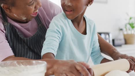 Happy-african-american-grandmother-and-granddaughter-baking-in-kitchen,-rolling-dough,-copy-space
