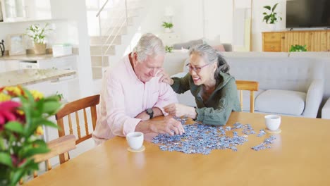 Happy-diverse-senior-couple-sitting-at-table-and-doing-puzzle