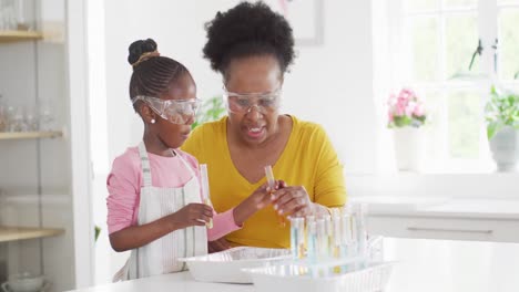 Excited-african-american-granddaughter-and-grandmother-make-chemistry-experiment-at-home,-copy-space