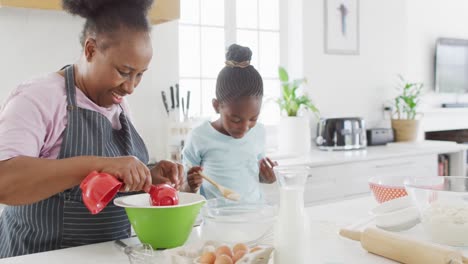 Happy-african-american-grandmother-and-granddaughter-having-fun-baking-in-kitchen,-copy-space