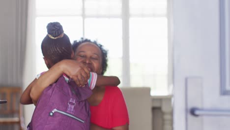 Video-of-african-american-granddaughter-with-schoolbag-coming-home-and-hugging-happy-grandmother