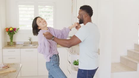 Happy-diverse-couple-holding-hands-and-dancing-in-kitchen