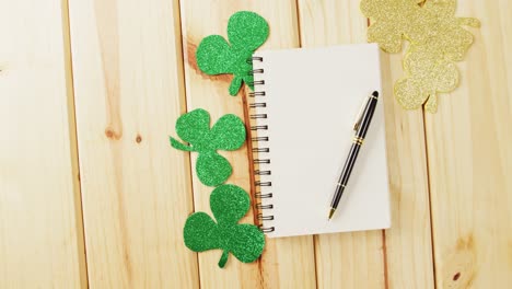 Video-of-st-patrick's-green-shamrock-and-notebook-with-copy-space-on-wooden-background