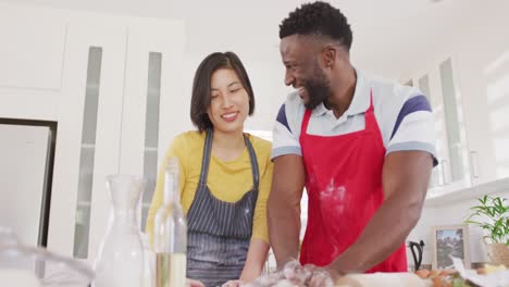 Happy-diverse-couple-wearing-aprons-and-baking-in-kitchen
