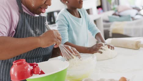Happy-african-american-grandmother-baking-with-granddaughter-kneading-dough,-in-kitchen,-copy-space