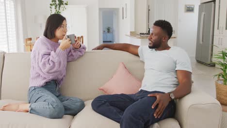 Diverse-couple-sitting-on-couch-and-drinking-coffee-in-living-room