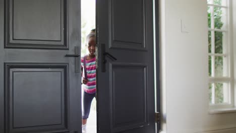 Video-of-african-american-girl-with-schoolbag-opening-front-door,-coming-home-from-school