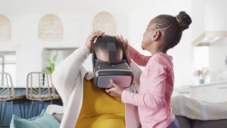 Happy-african-american-granddaughter-putting-vr-headset-on-grandmother-at-home,-copy-space