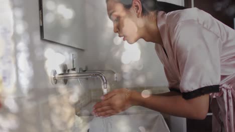 Animation-of-glowing-lights-over-biracial-woman-washing-face