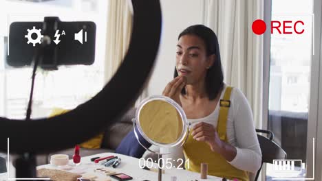 Animation-of-digital-interface-and-icons-over-biracial-woman-on-makeup-vlog