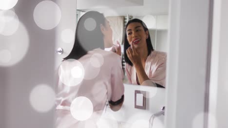 Animation-of-light-spots-over-biracial-woman-applying-lipstick