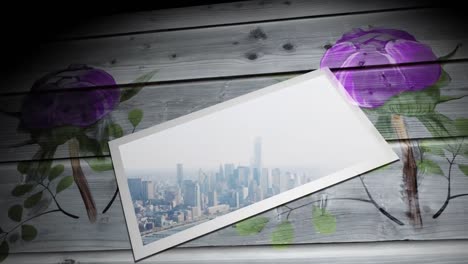 Animation-of-modern-cityscape-in-white-frame-and-purple-flowers-on-wooden-table