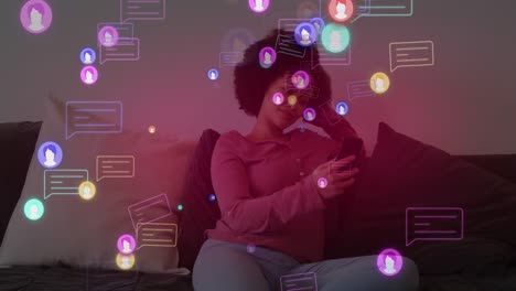 Animation-of-social-media-icons-with-speech-bubbles-over-african-american-woman-using-smartphone