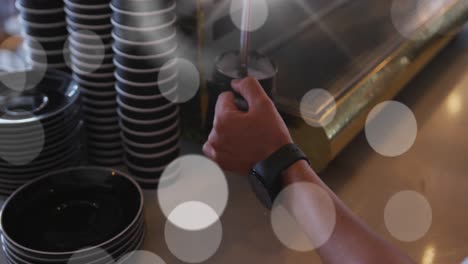 Animation-Von-Lichtflecken-über-Einem-Mann,-Der-Im-Café-Kaffee-Kocht