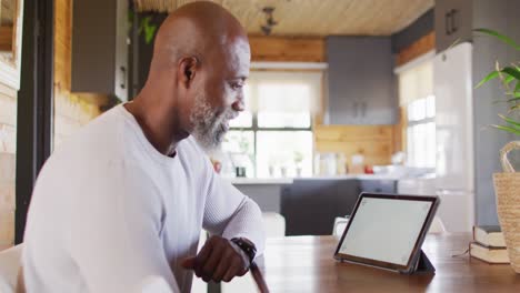 Happy-senior-african-american-man-sitting-at-table-and-using-tablet-with-copy-space,-slow-motion
