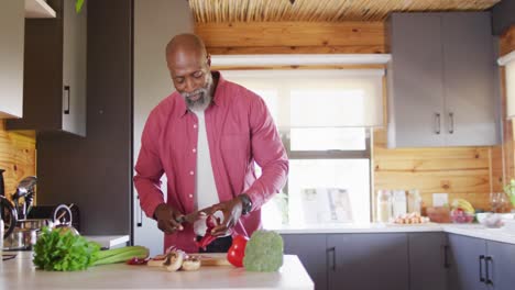 Happy-senior-african-american-man-spending-time-in-log-cabin,-cooking-in-kitchen