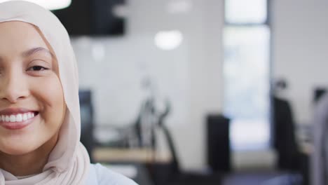 Portrait-of-happy-biracial-businesswoman-wearing-hijab-in-office,-slow-motion