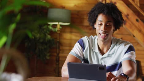 Happy-african-american-man-sitting-at-table-and-using-tablet-for-video-call,-slow-motion