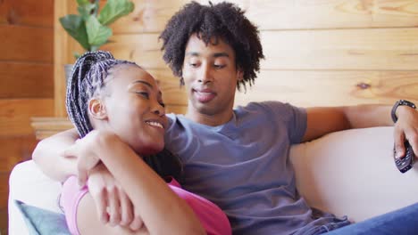 Happy-african-american-couple-watching-tv,-sitting-on-sofa-in-log-cabin,-slow-motion