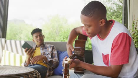 Happy-african-american-male-teenage-friends-playing-guitar-at-home,-slow-motion