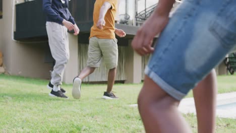 Happy-diverse-male-teenage-friends-playing-football-in-garden,-slow-motion