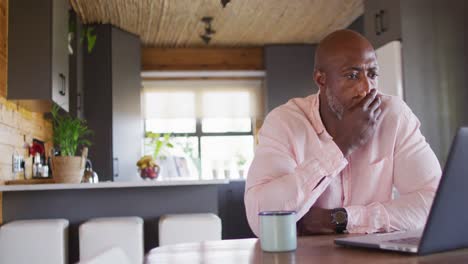 Senior-african-american-man-in-log-cabin,-sitting-at-table-and-using-laptop,-slow-motion