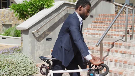 Happy-african-american-businessman-going-up-stairs-with-bike,-slow-motion