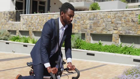 Happy-african-american-businessman-riding-bike-at-street,-slow-motion