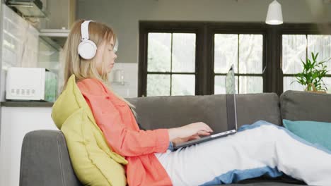 A-caucasian-teenager-girl-with-headphones-using-laptop-at-home,-slow-motion