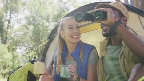 Happy-diverse-couple-camping,-drinking-tea-and-using-binoculars-in-park,-slow-motion