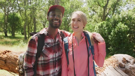 Portrait-of-happy-diverse-couple-with-backpacks-embracing-in-park,-slow-motion