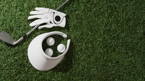 Close-up-of-golf-club,-balls,-glove-and-peaked-cap-on-grass,-copy-space,-slow-motion