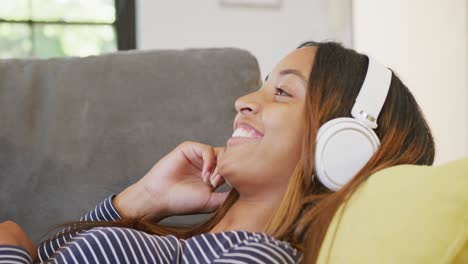 A-happy-biracial-teenager-girl-with-headphones-smiling-at-home,-slow-motion