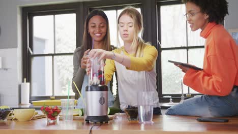 Happy-diverse-teenager-girls-friends-preparing-healthy-drink-using-tablet-in-kitchen,-slow-motion